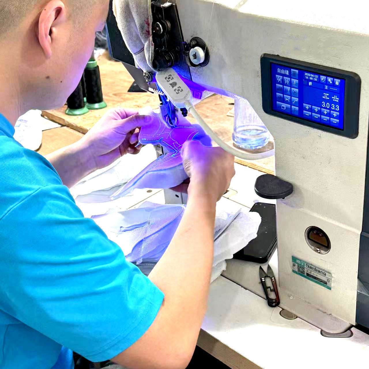 Person using a sewing machine with a digital display in a workshop setting.
